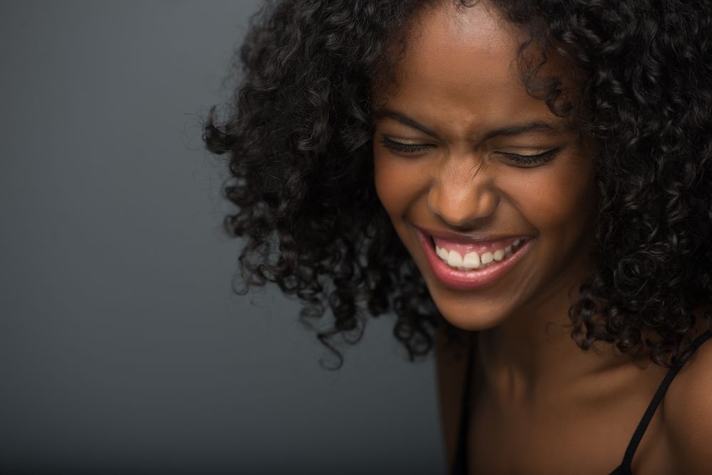 A person with curly natural hair and bright red lipstick smiles joyfully while looking to the side.