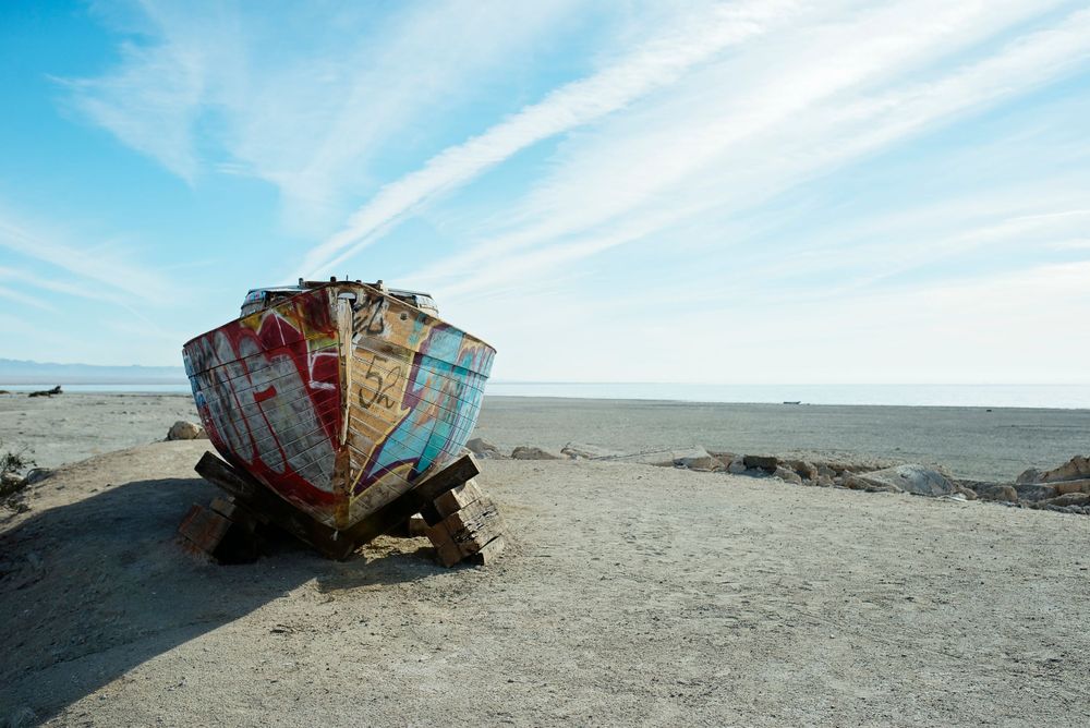 Old weathered fishing boat abandoned on beach under bright blue sky.