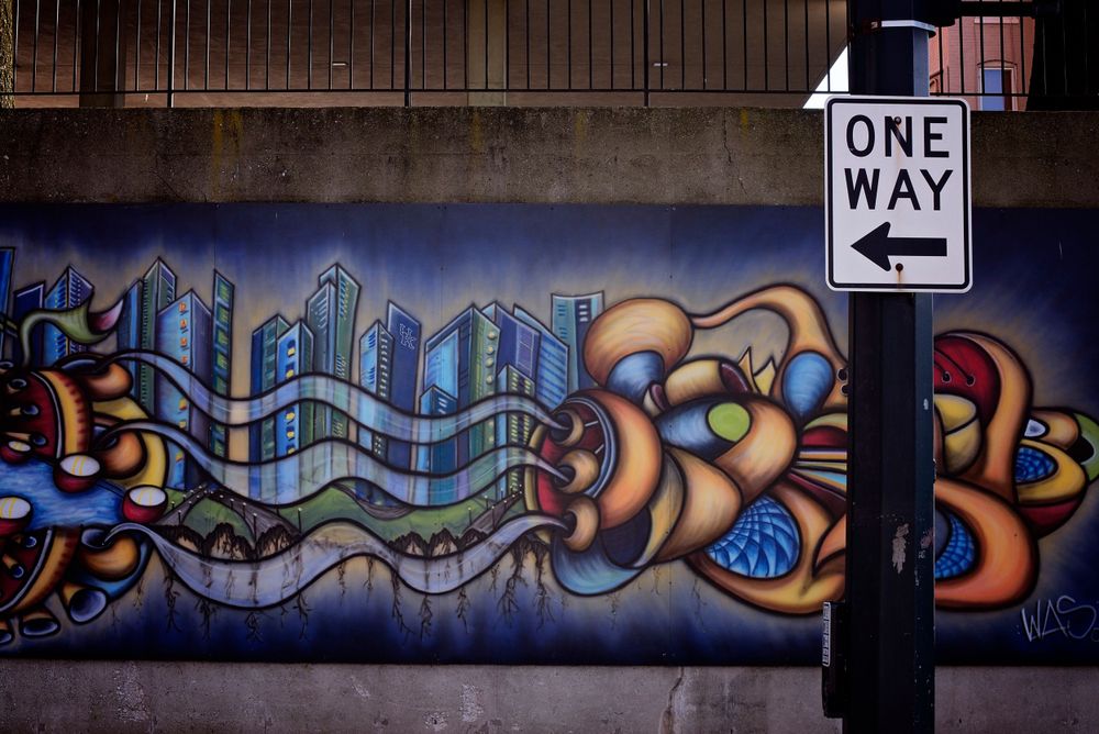 Colorful graffiti mural depicting city skyline with one-way sign in urban setting.