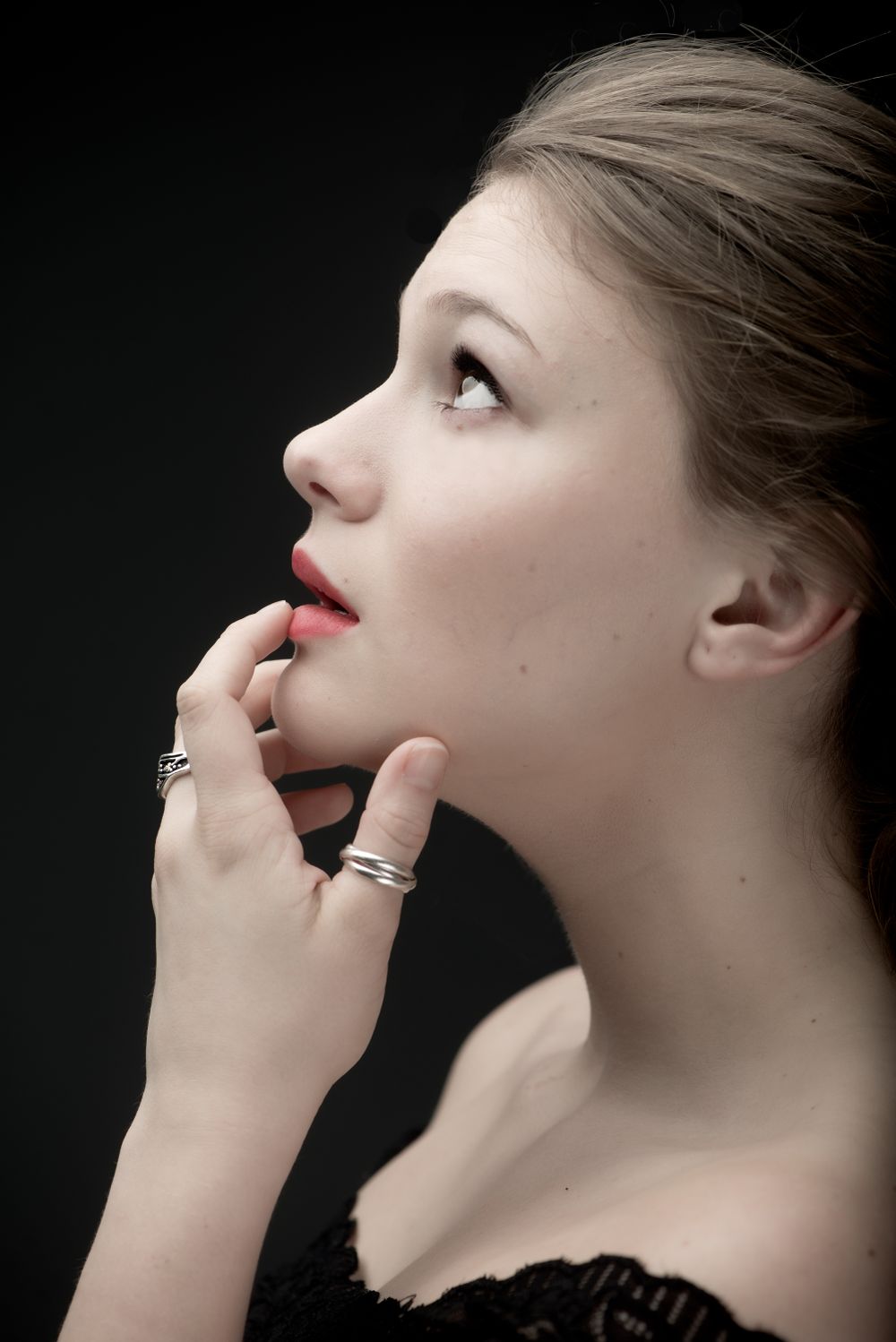 Elegant profile portrait with red lips and rings against dark backdrop.