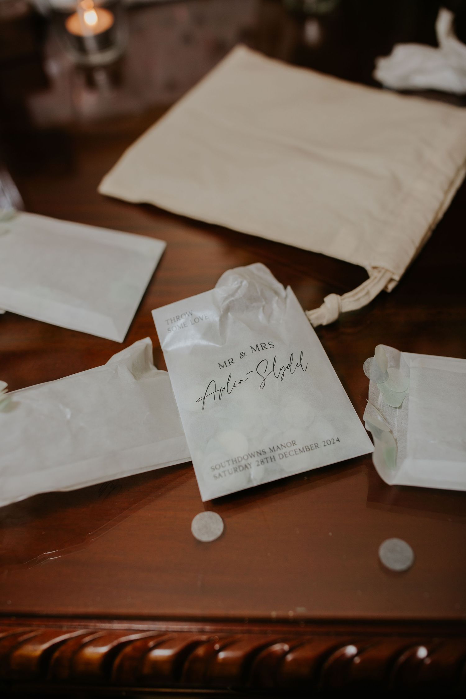 Small white favor bags and envelopes scattered on brown leather surface with handwritten details visible.