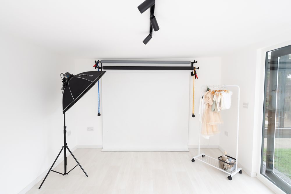 Professional photography studio setup with white backdrop, lighting equipment and stands against clean white walls.