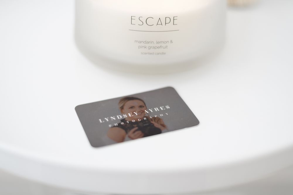A blurred loyalty card or gift card sits on a white surface next to what appears to be a candle or cosmetic jar.