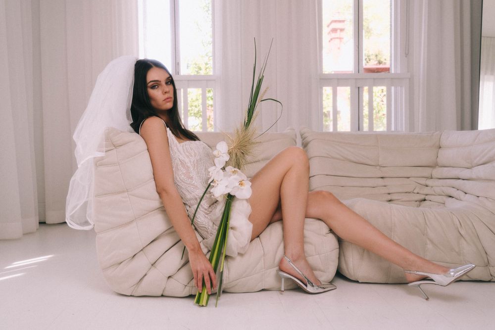 Elegant bridal pose on cream couch with dried palm fronds and white veil.