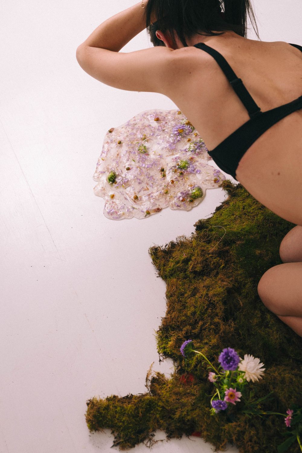 Artistic photo composition with moss, flowers and black swimwear against white background.