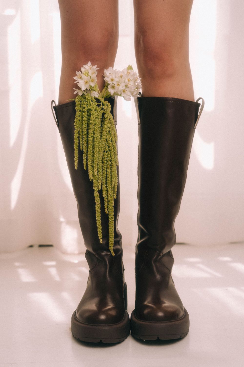Black knee-high boots decorated with cascading white flowers and greenery.