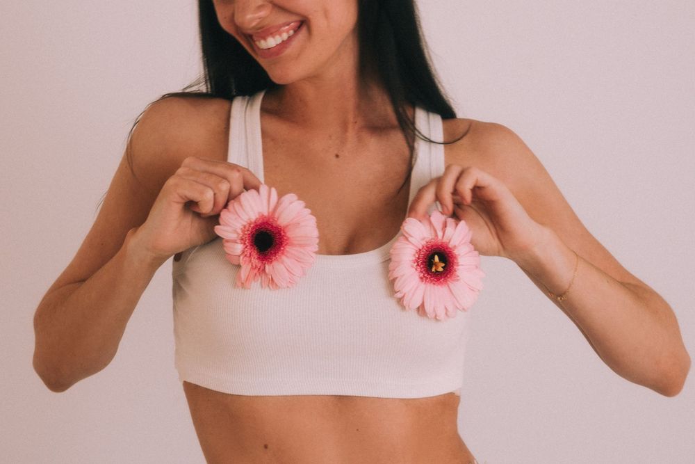 Pink gerbera daisies held against white crop top in fashion photography.