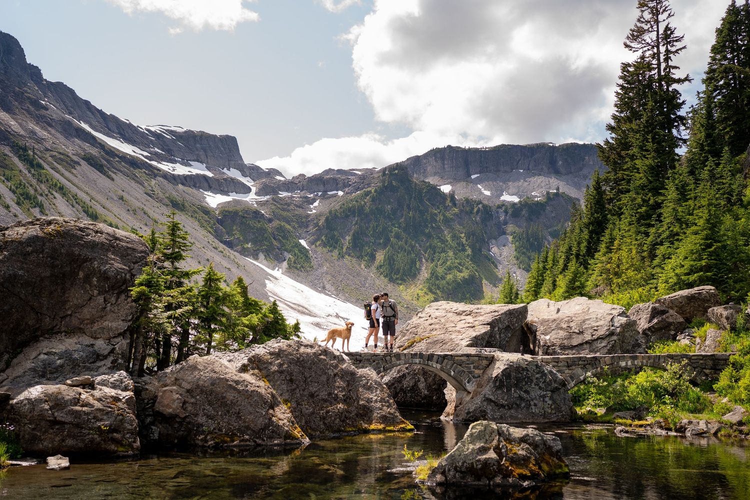 A mountain lake scene with rocky outcrops and snow patches in the distance.