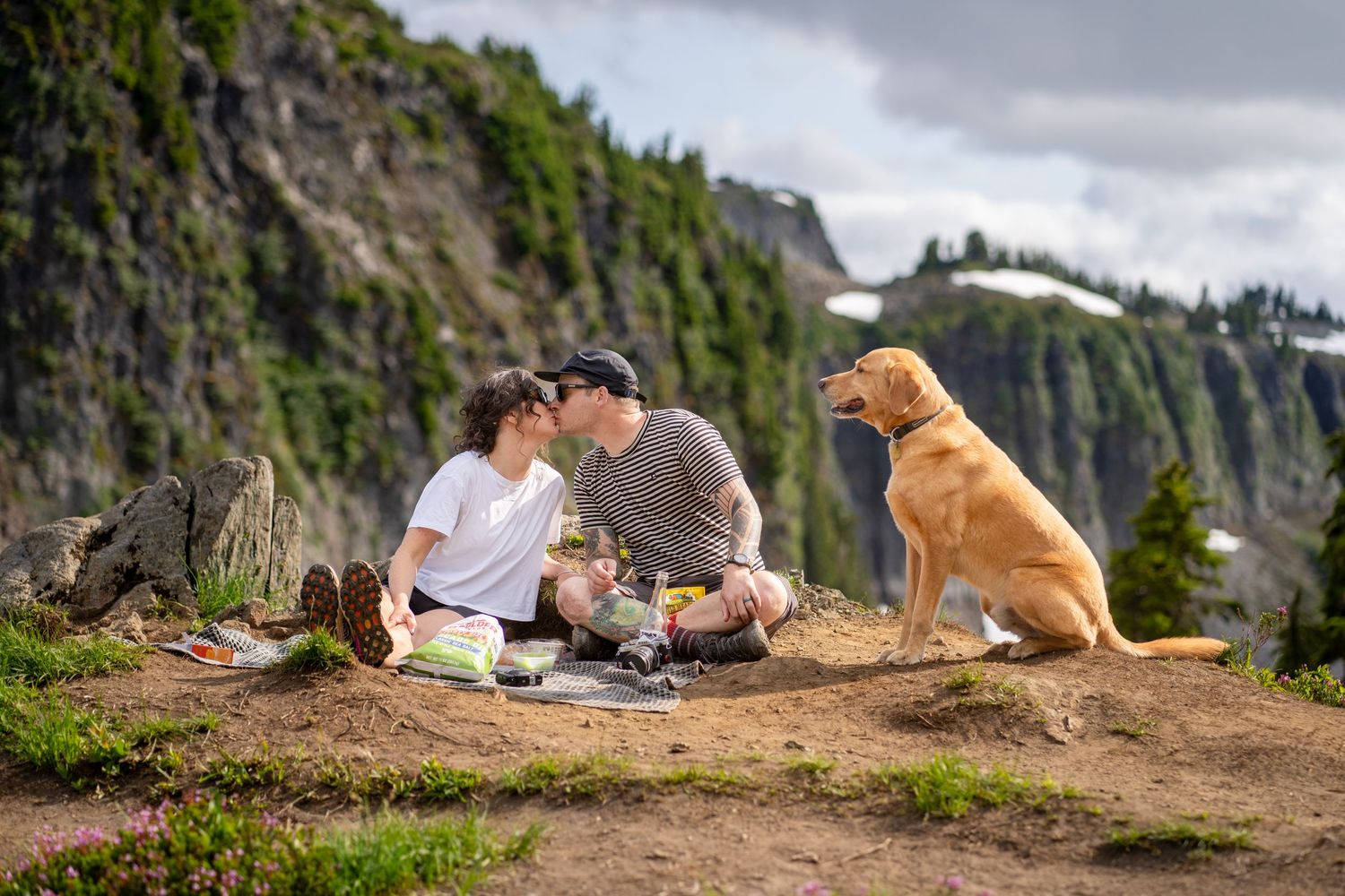 A golden retriever joins a couple for a picnic on a mountain overlook.