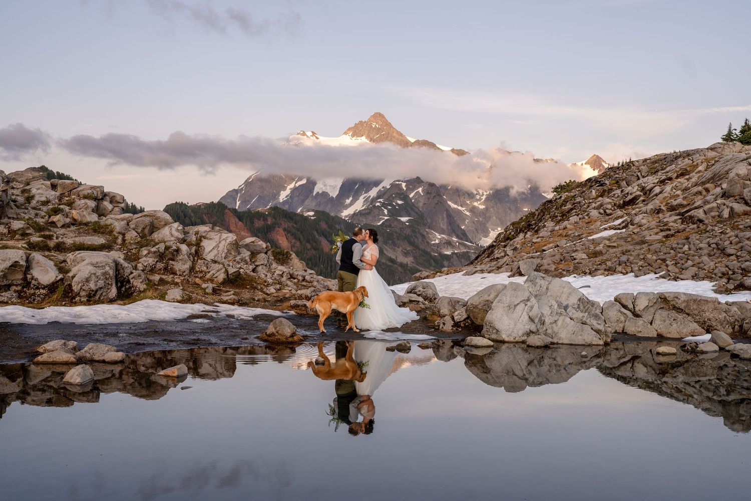 A mountain lake reflects the sunset glow on rocky terrain with peaks in the distance.