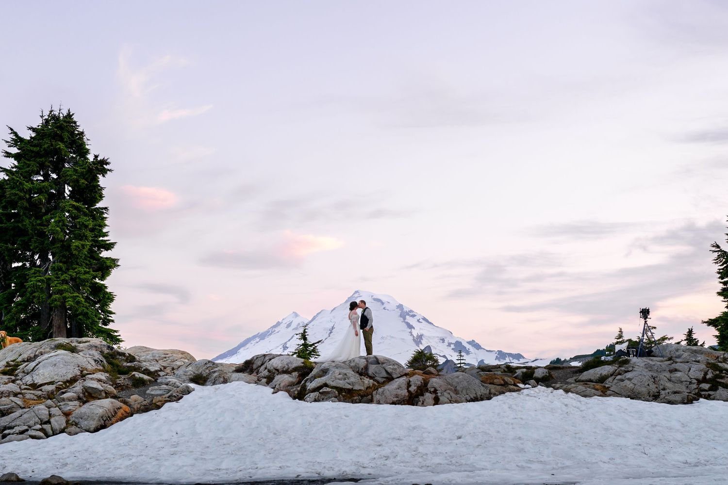 Silhouettes pose against snowy mountain backdrop during sunset wedding photoshoot.