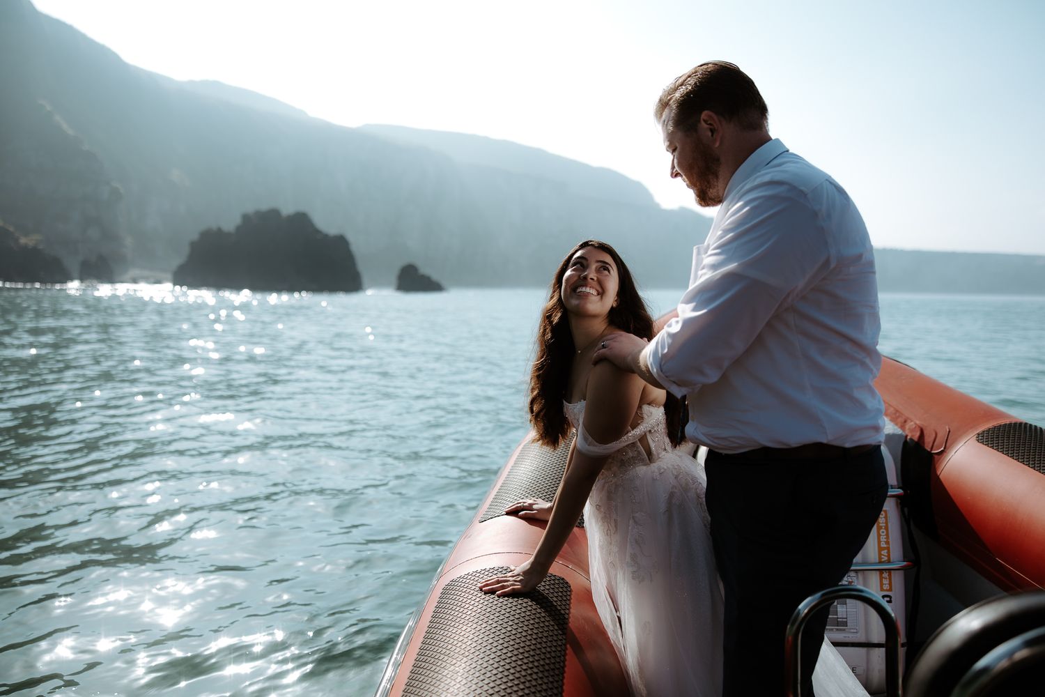 A couple shares an intimate moment on a boat with dramatic coastal cliffs in the background.