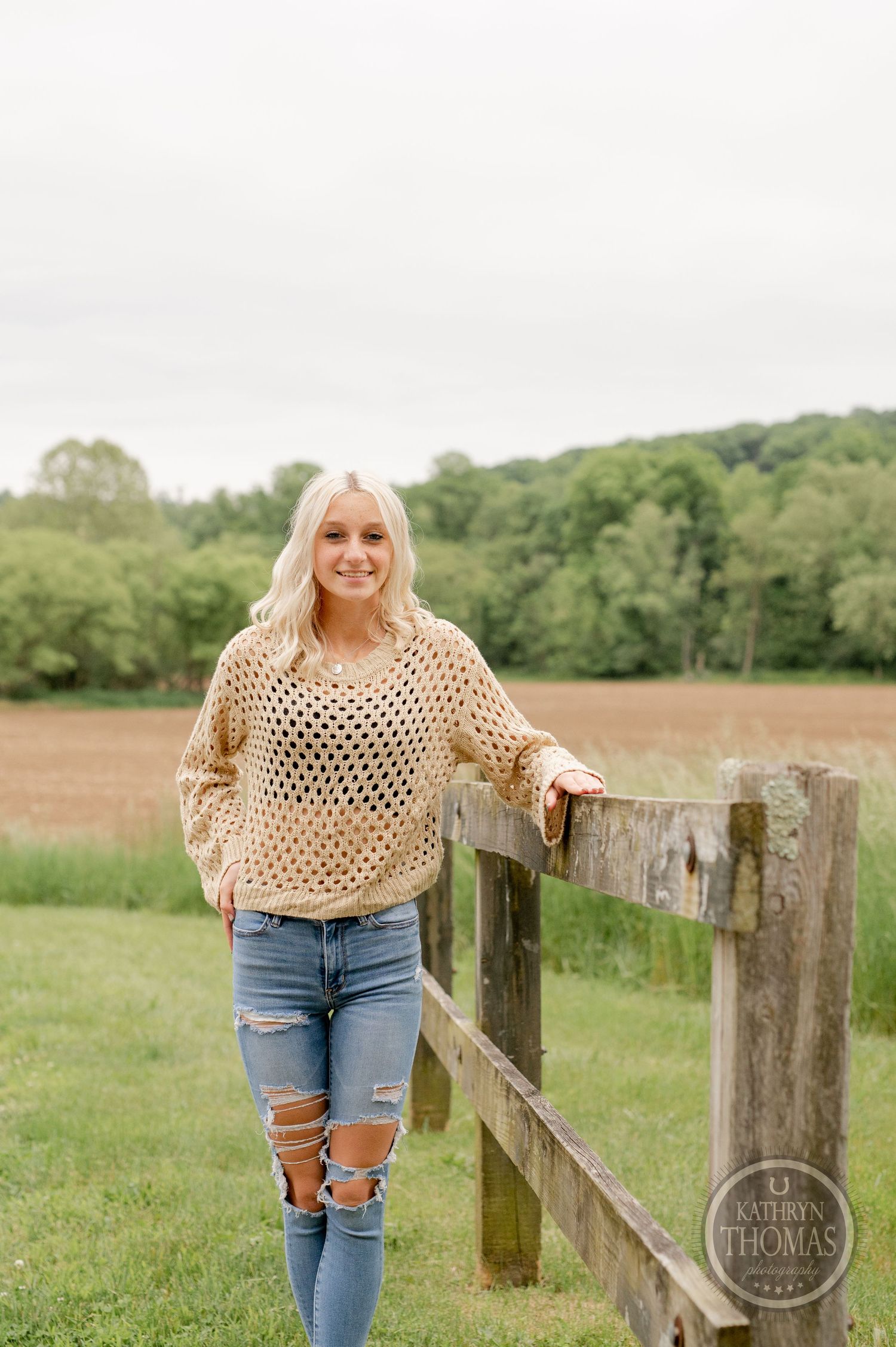 Country fashion look with distressed jeans and beige sweater by rustic wooden fence.