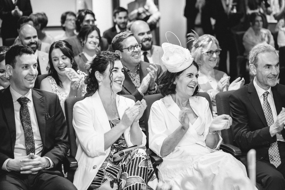 Black and white photo of wedding guests laughing and clapping during a ceremony.