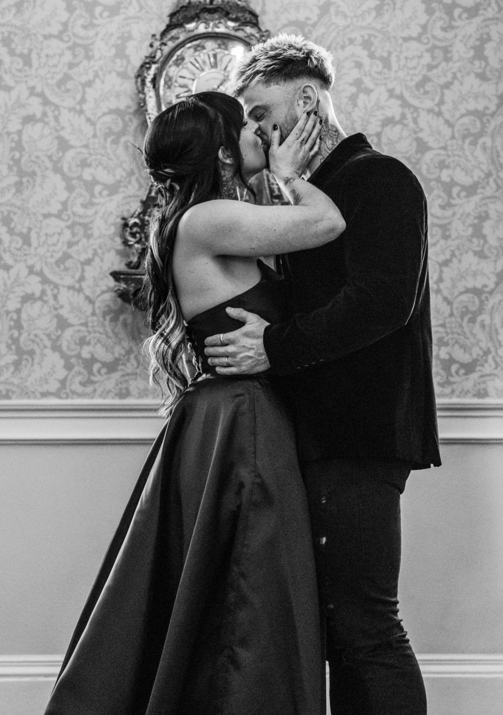 A romantic black and white photo of a couple sharing an intimate embrace against a damask wallpaper background.