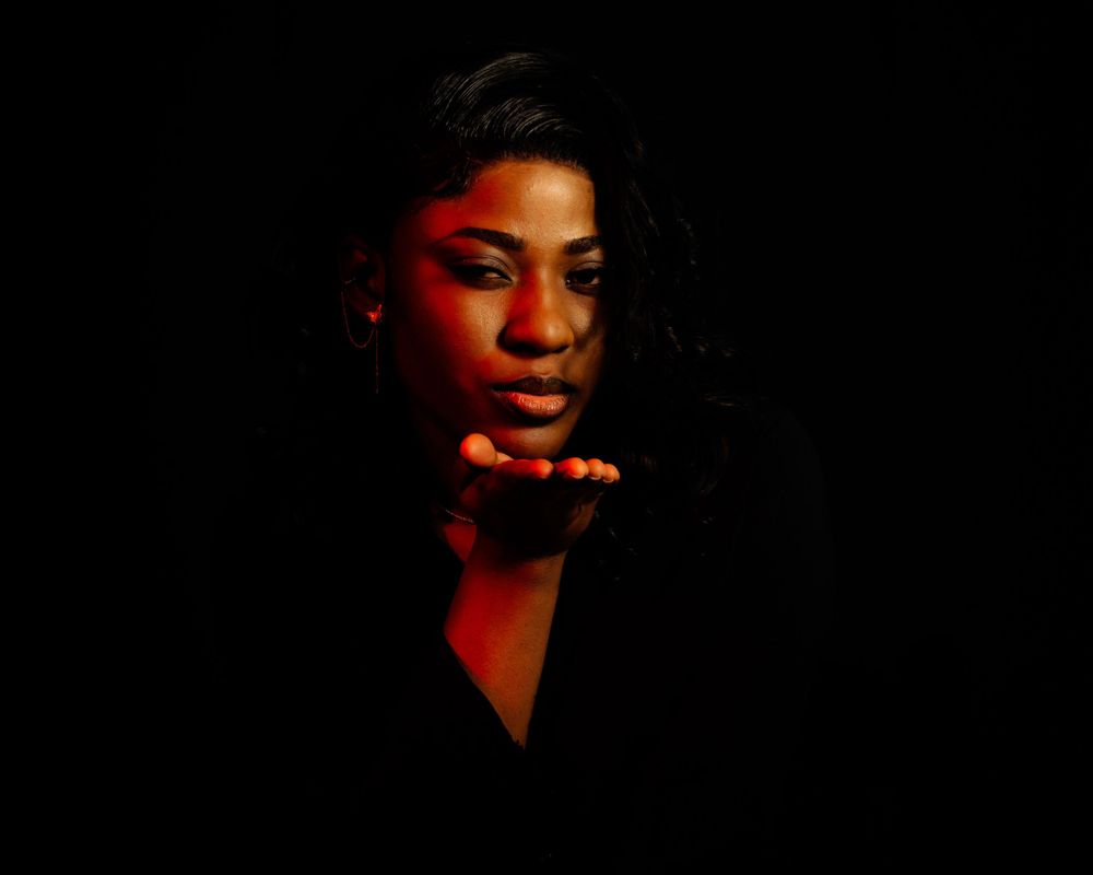 A dramatic portrait illuminated by red lighting against a dark background shows a person captured in an atmospheric moment.