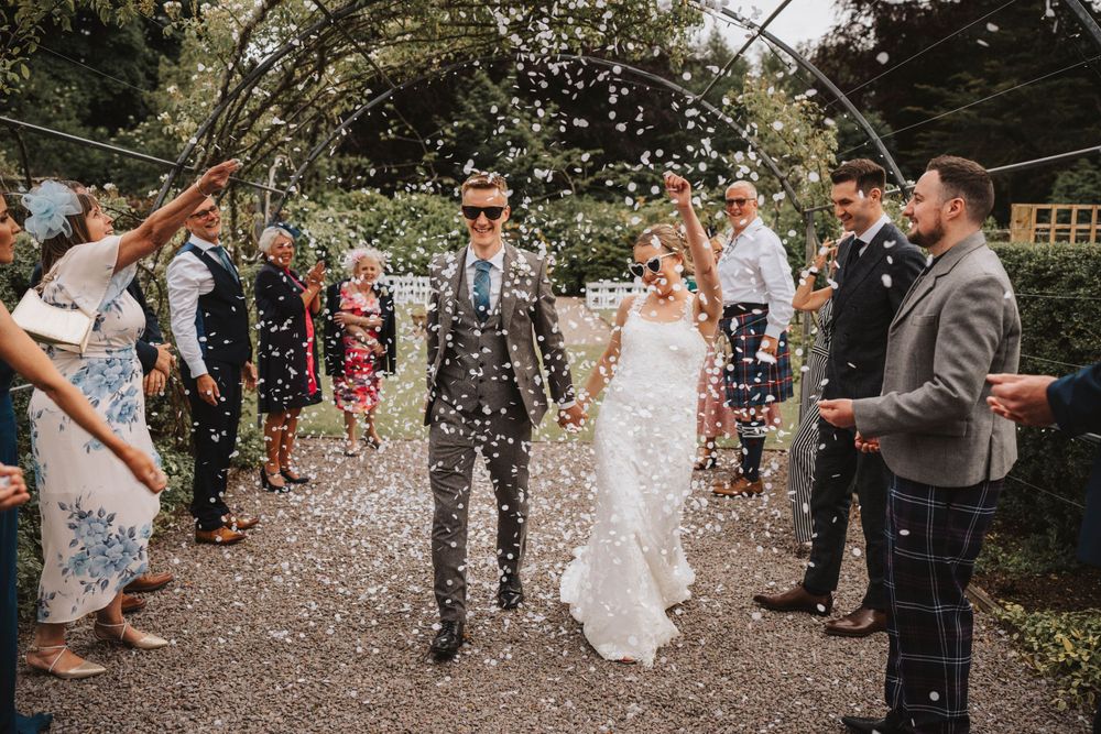 Wedding couple walks through shower of confetti with guests on garden path at elsick house Aberdeenshire.