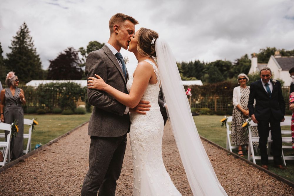 A wedding ceremony on a gravel path with guests seated on either side having their first kiss at elsick house Aberdeenshire.