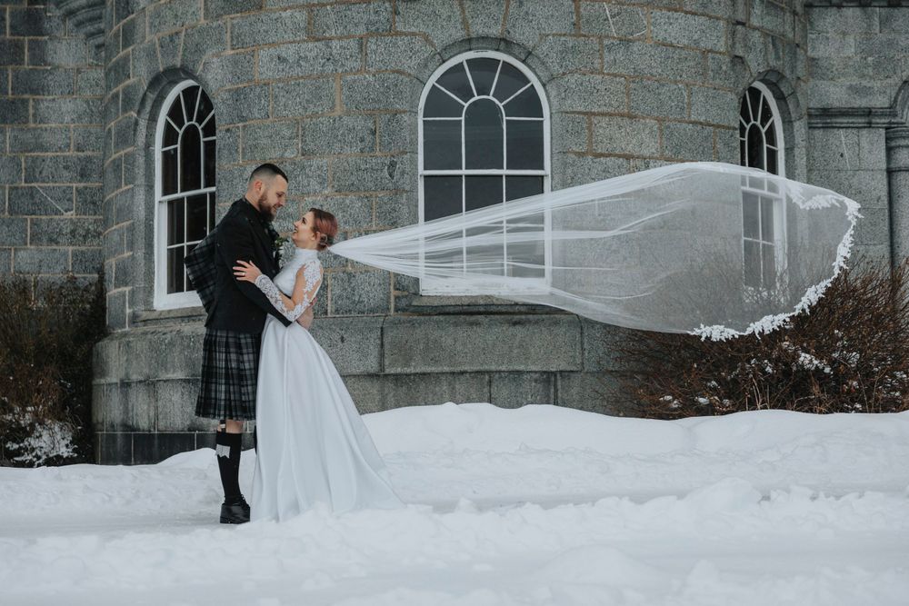 A dramatic winter wedding photo with flowing veil against snowy backdrop at Cluny Castle Aberdeenshire.