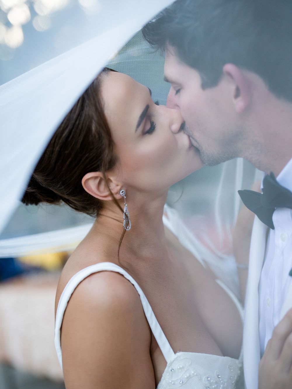 Romantic wedding moment captured under a delicate veil as couple shares an intimate kiss.
