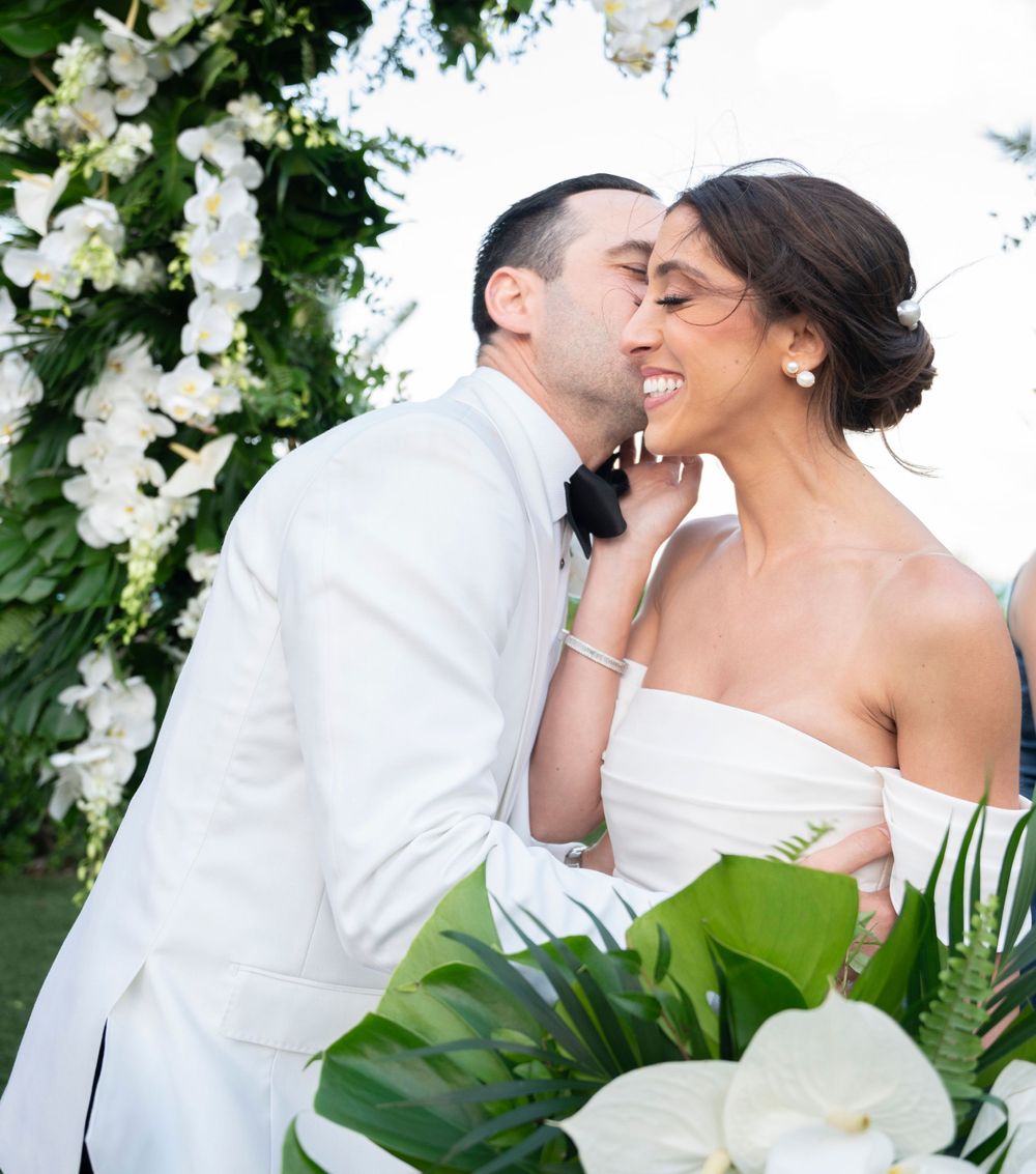Wedding couple shares intimate moment under floral arch with white orchids.