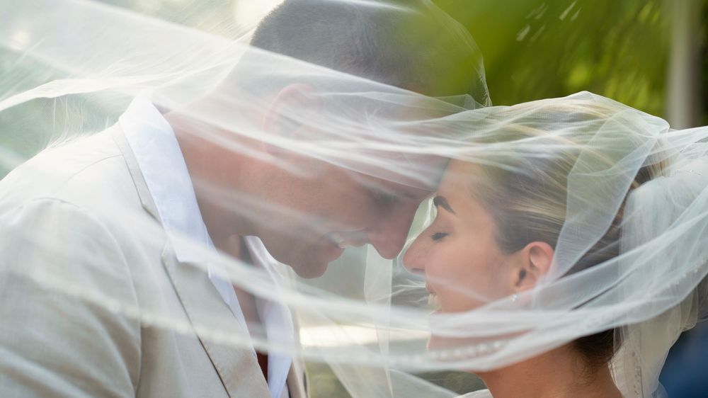 Bride and groom sharing a romantic kiss under a flowing white wedding veil outdoors.
