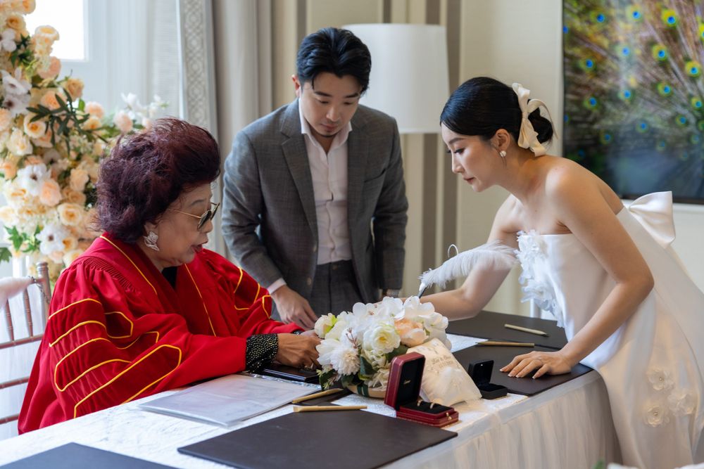 A wedding ceremony scene with people gathered around a table with documents and flowers.