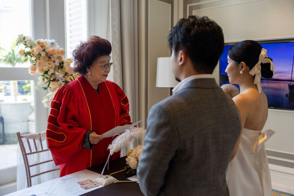 Wedding ceremony with officiant in red jacket conducting service under floral decorations.