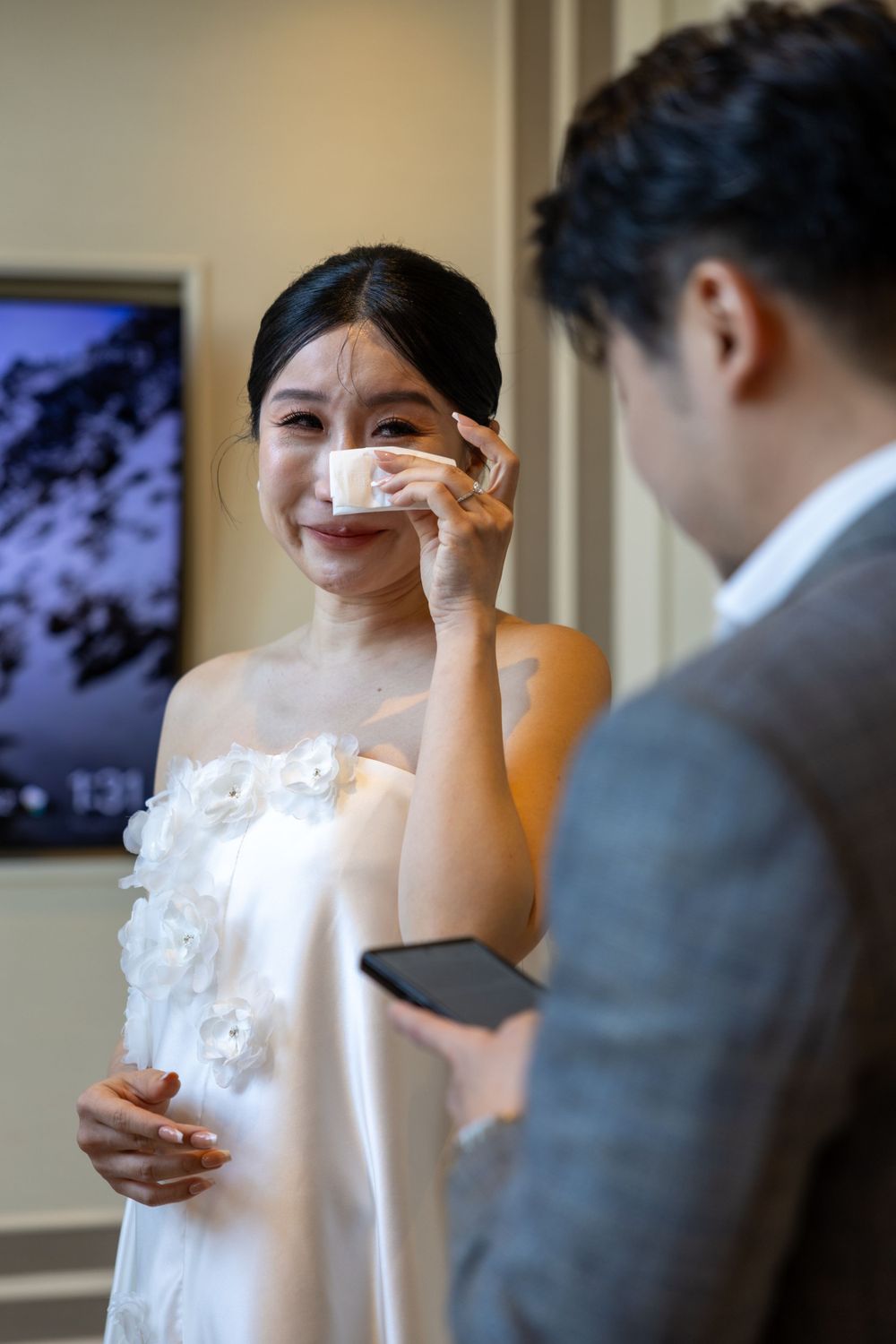An emotional wedding moment captured as someone wipes tears while wearing a white dress.