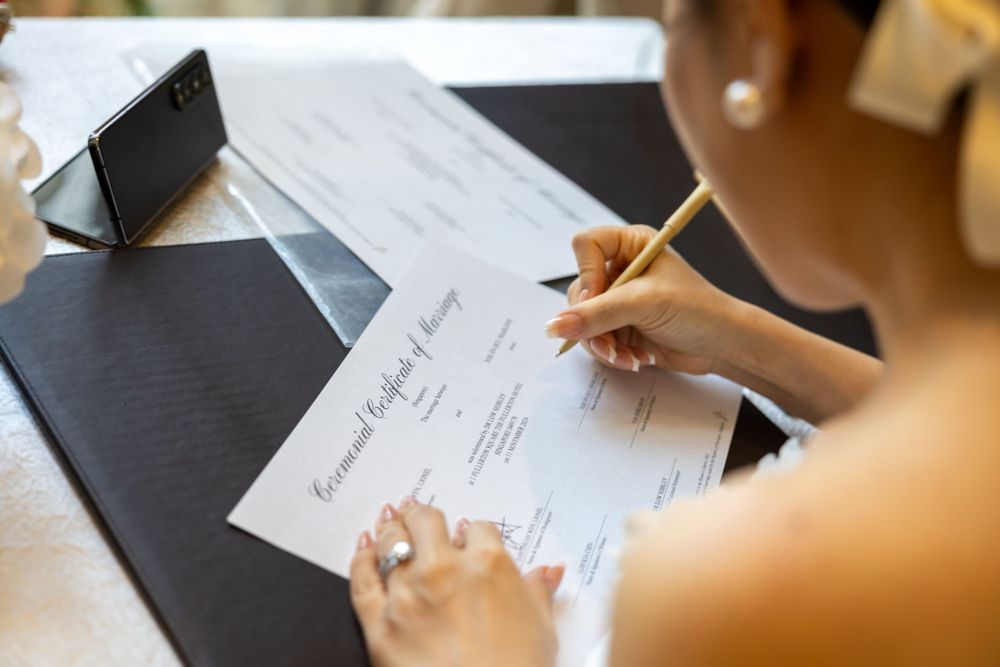 Close-up of hands signing wedding documentation on a black surface.