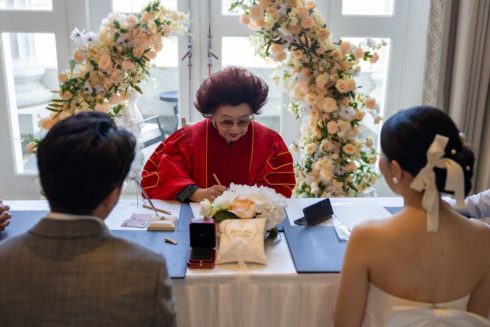 Wedding ceremony at an indoor venue with a floral arch and officiant in red presiding over the service.