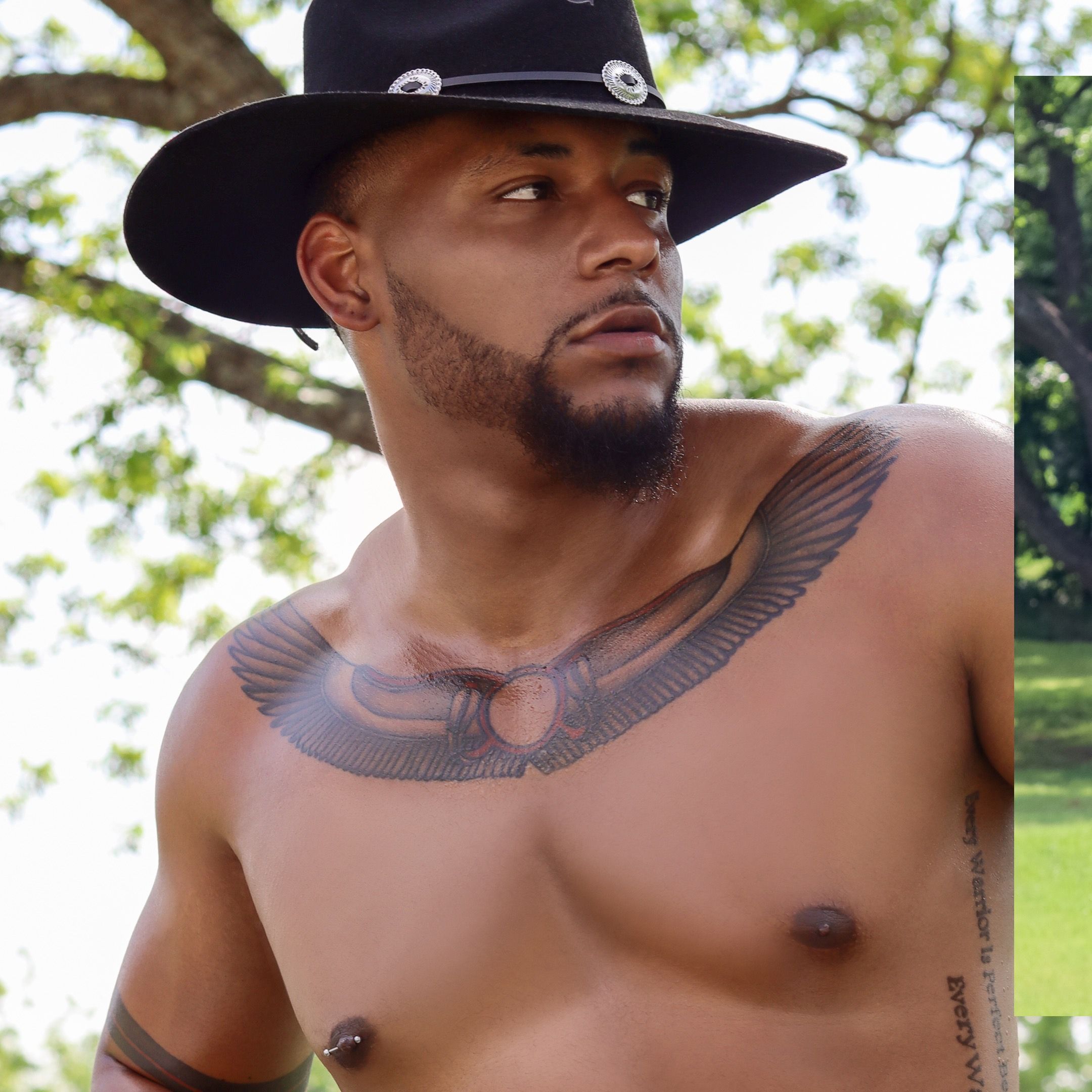 Athletic shirtless person wearing black cowboy hat with eagle wing chest tattoo poses outdoors in natural setting.
