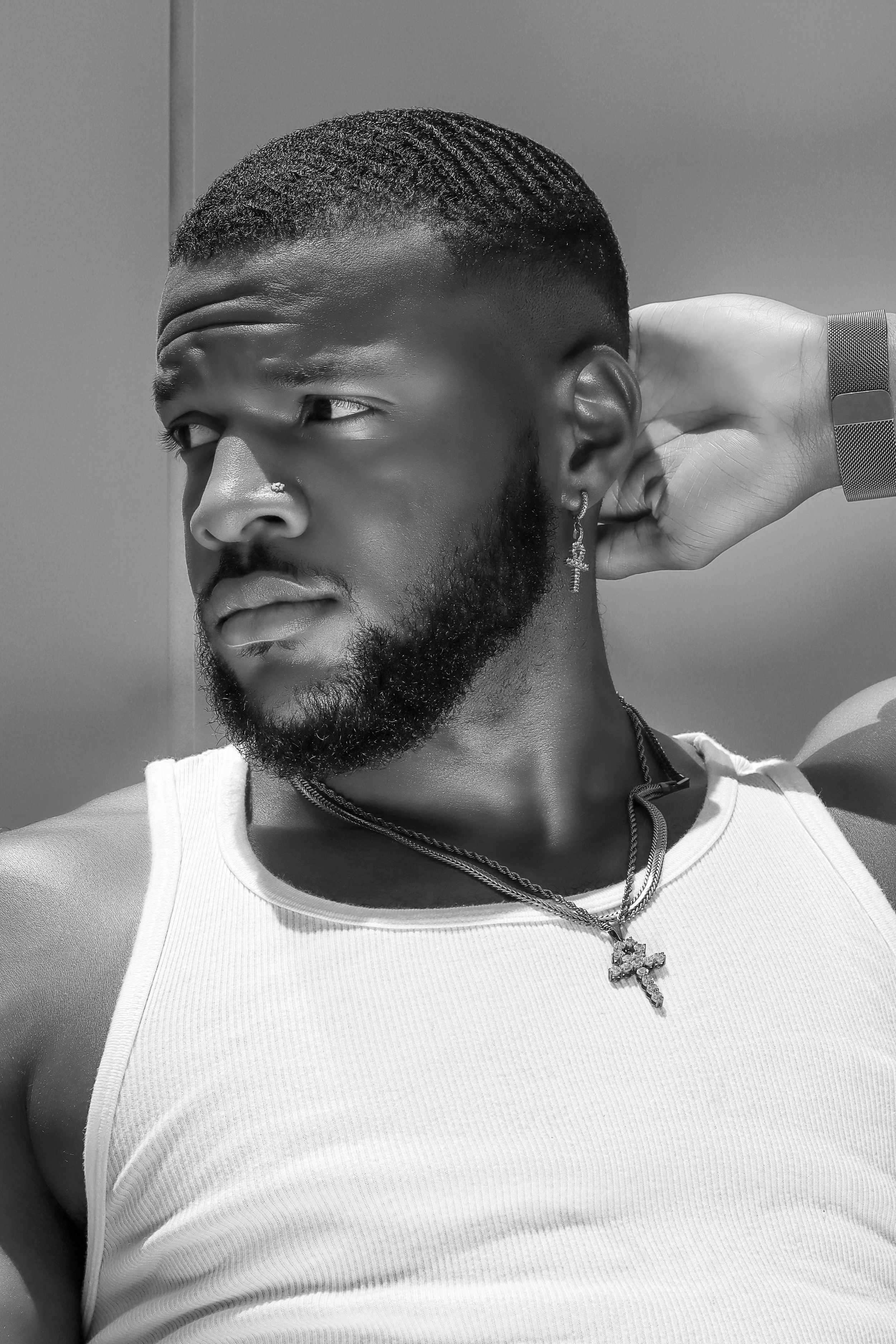 Black and white portrait showing cornrow hairstyle, white tank top, and cross necklace in dramatic side lighting.