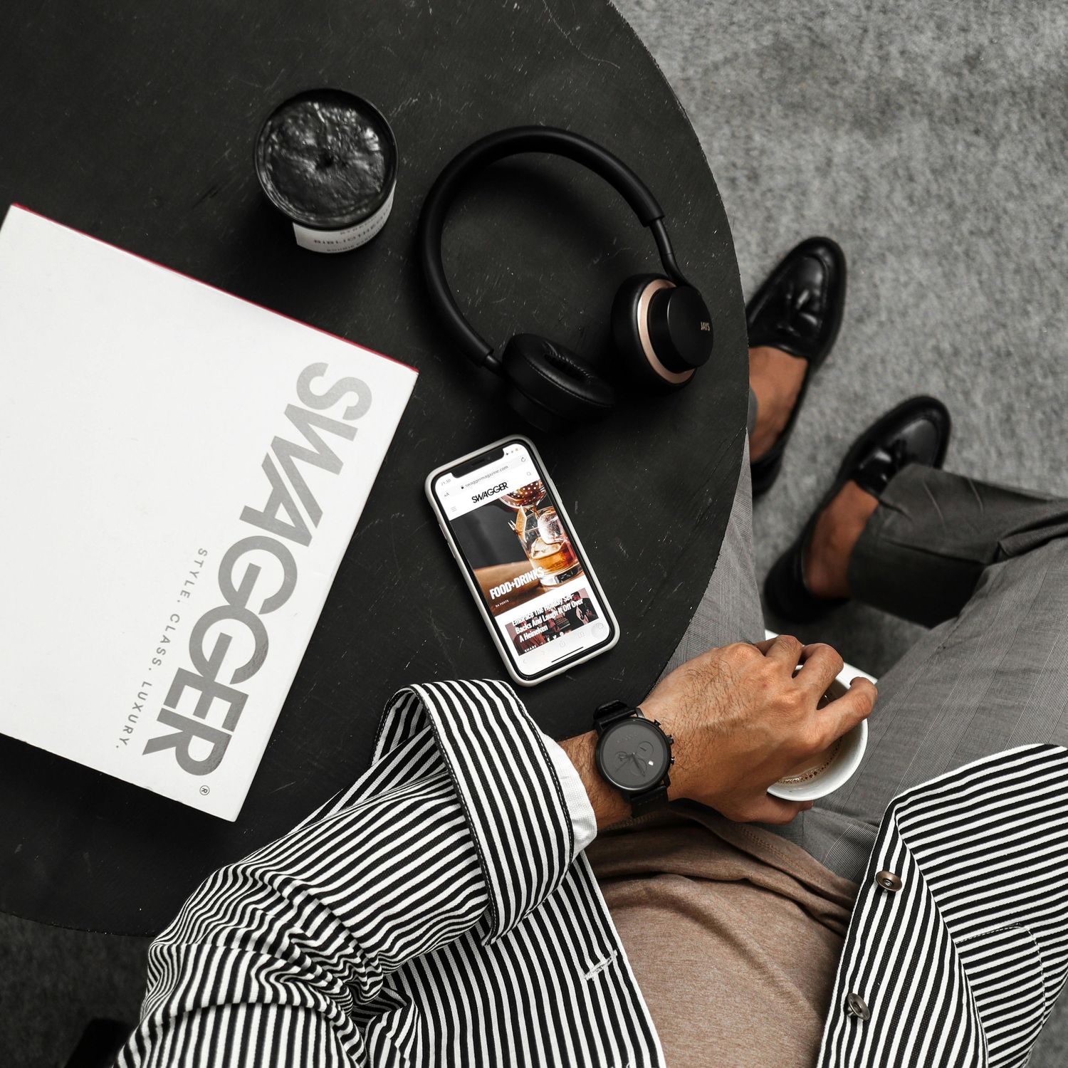 Overhead view of headphones, sneakers and striped outfit with phone on black table surface.