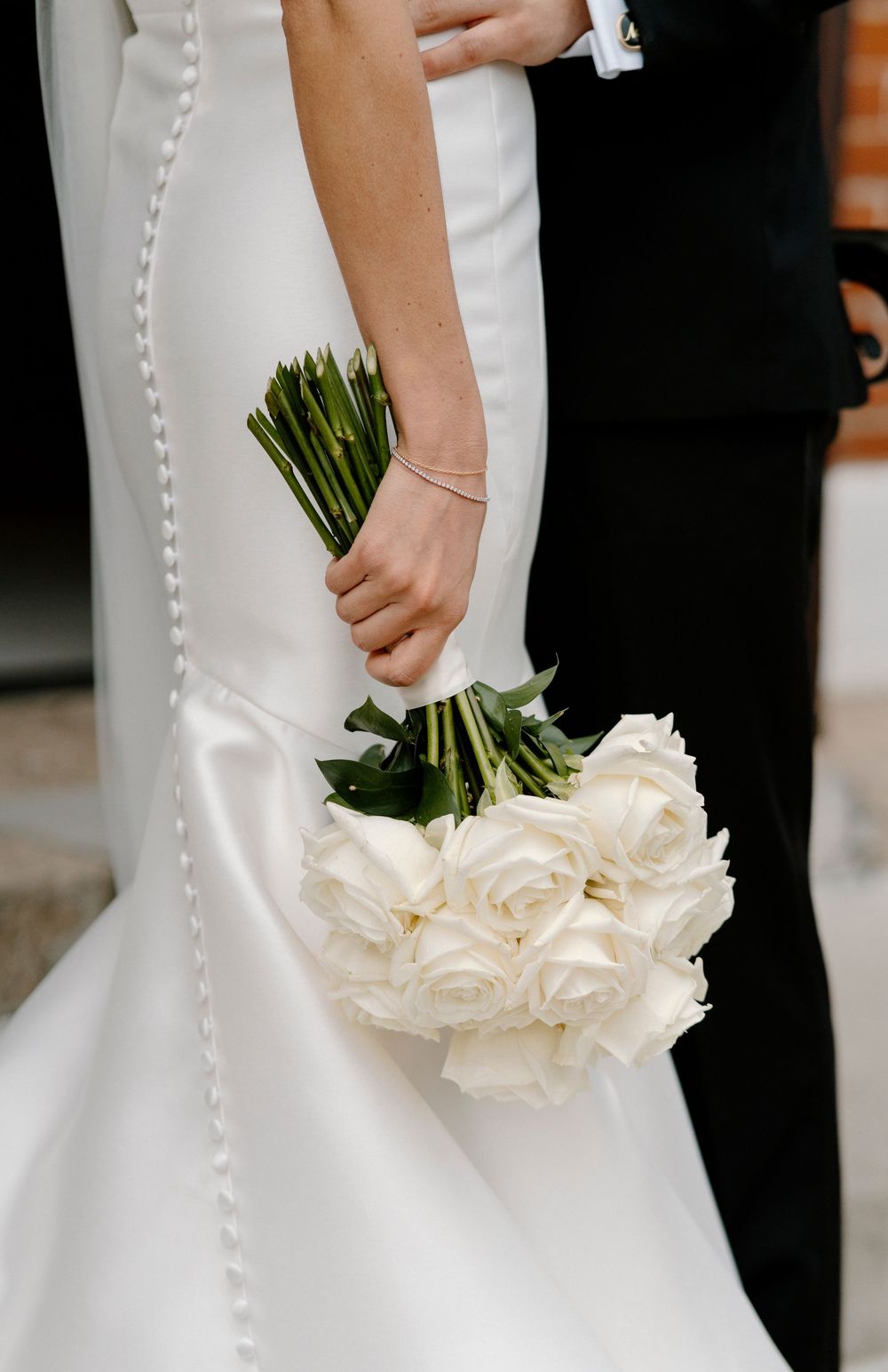 Close-up details of a white wedding dress with pearl buttons and bride holding an elegant bouquet of cream roses.