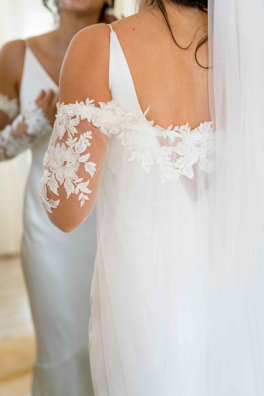 Close up detail of delicate white floral lace applique on sheer long sleeve wedding dress.