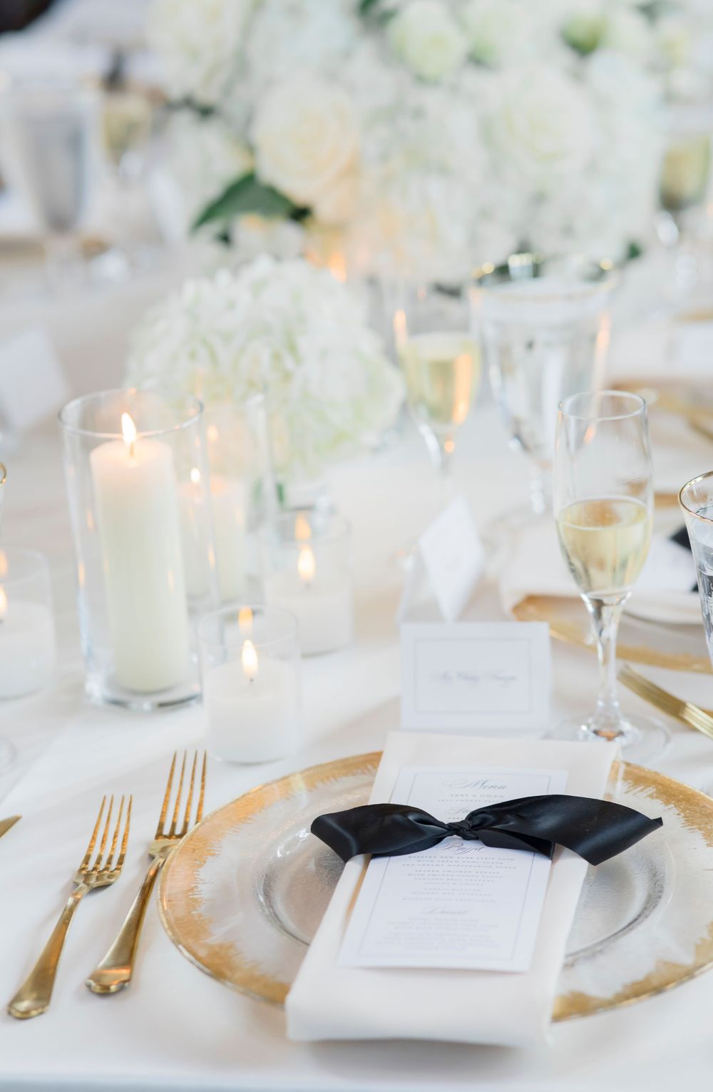 Elegant white and gold place settings with lit candles create a luxurious wedding reception tablescape.