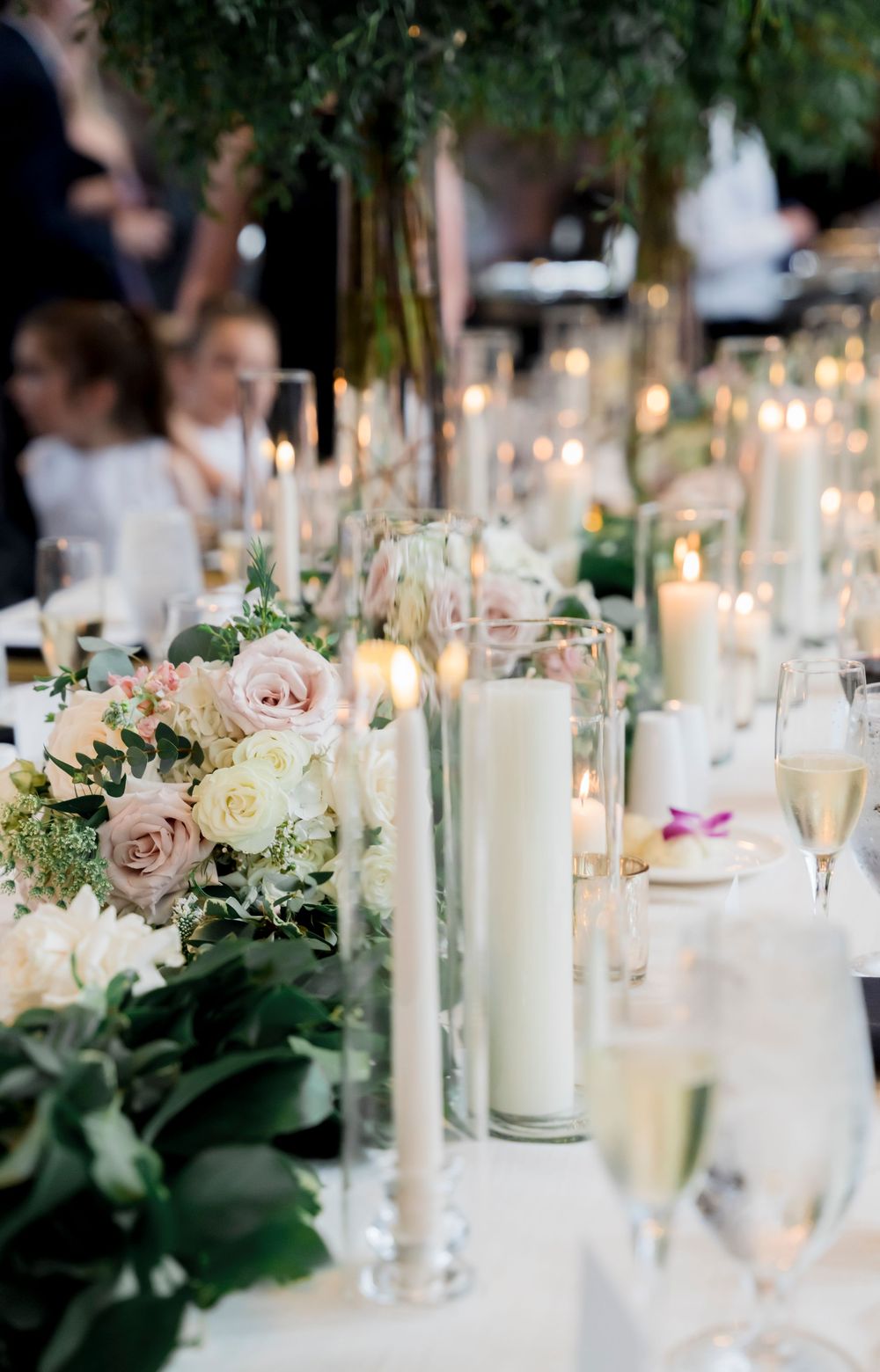 Elegant wedding reception table decorated with blush roses, white candles and champagne glasses creating a romantic ambiance.