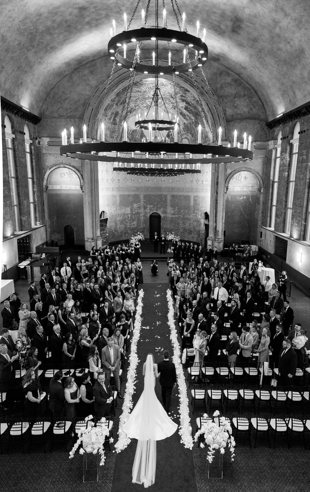 A striking black and white aerial view of a wedding ceremony in a grand church with vaulted ceilings and chandeliers.