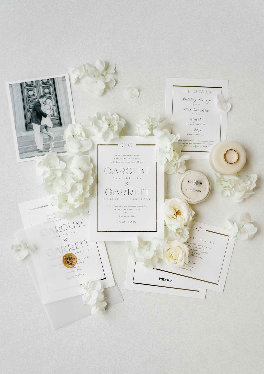 Elegant white wedding invitation suite with fresh hydrangea petals and vintage photograph on light background.