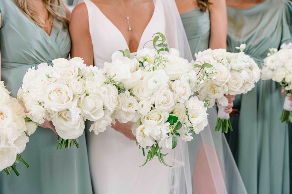 Row of elegant white rose bouquets held against sage green bridesmaid dresses.