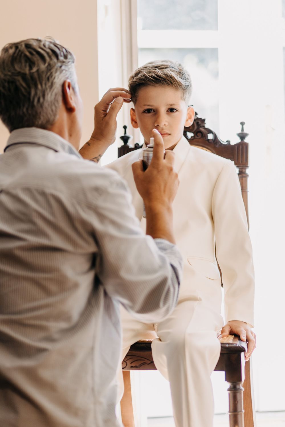A young person in a white suit being helped with prepping for a formal occasion.