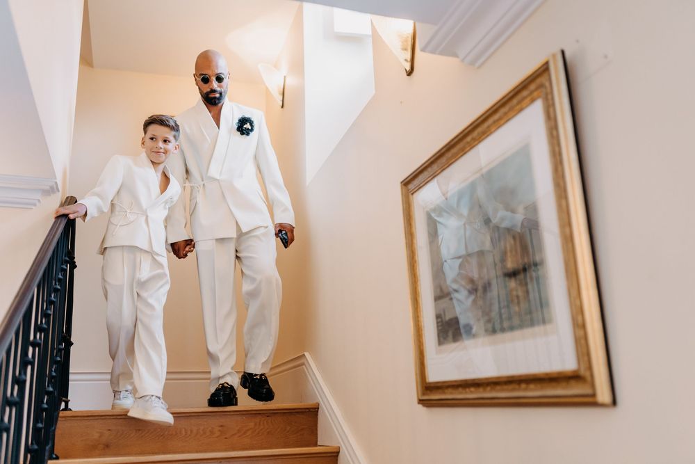 Two people in matching white outfits descending an elegant staircase with a framed artwork on the wall.