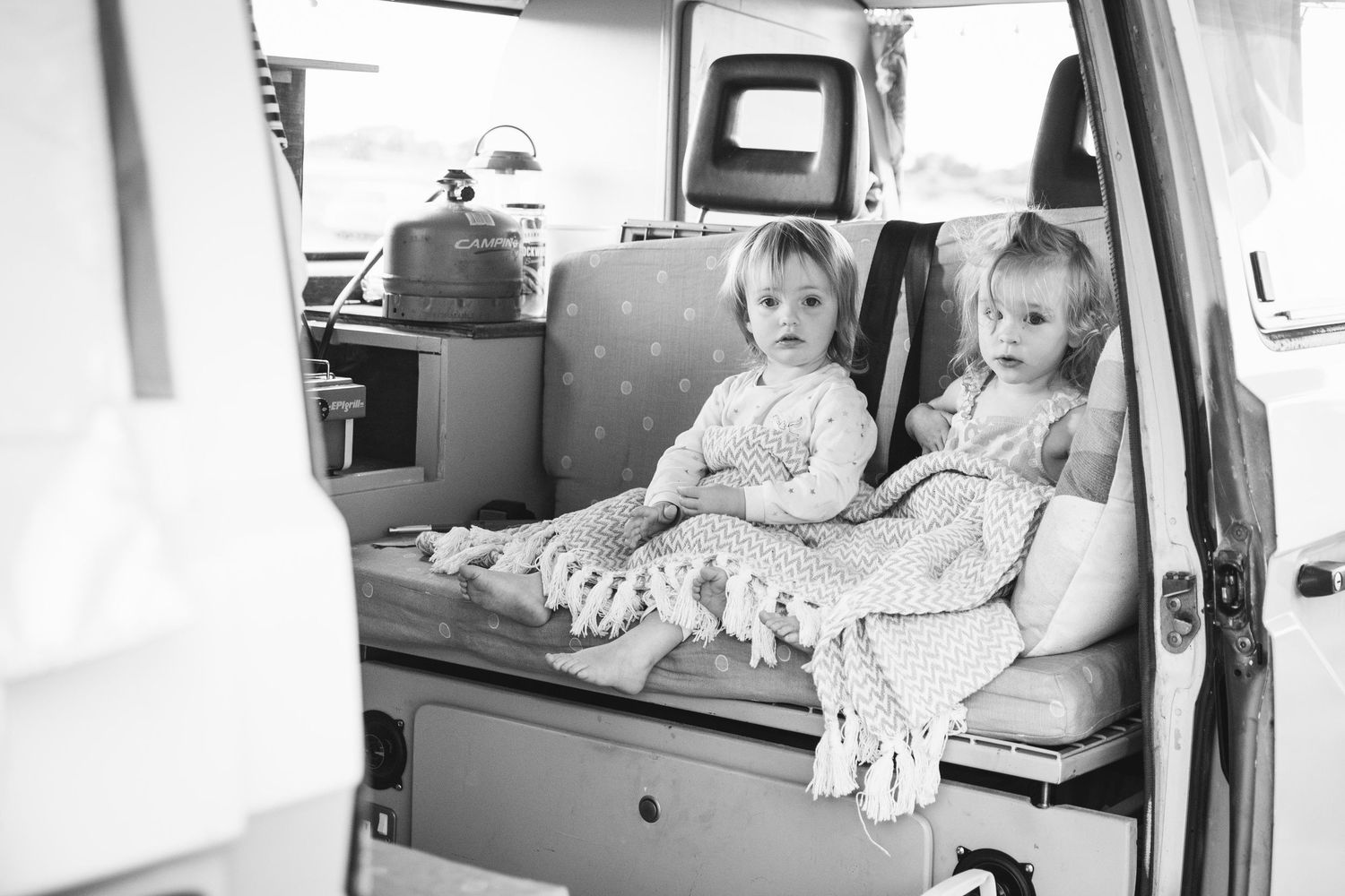 Two small children sit together in black and white on the back seat of a classic vehicle interior.