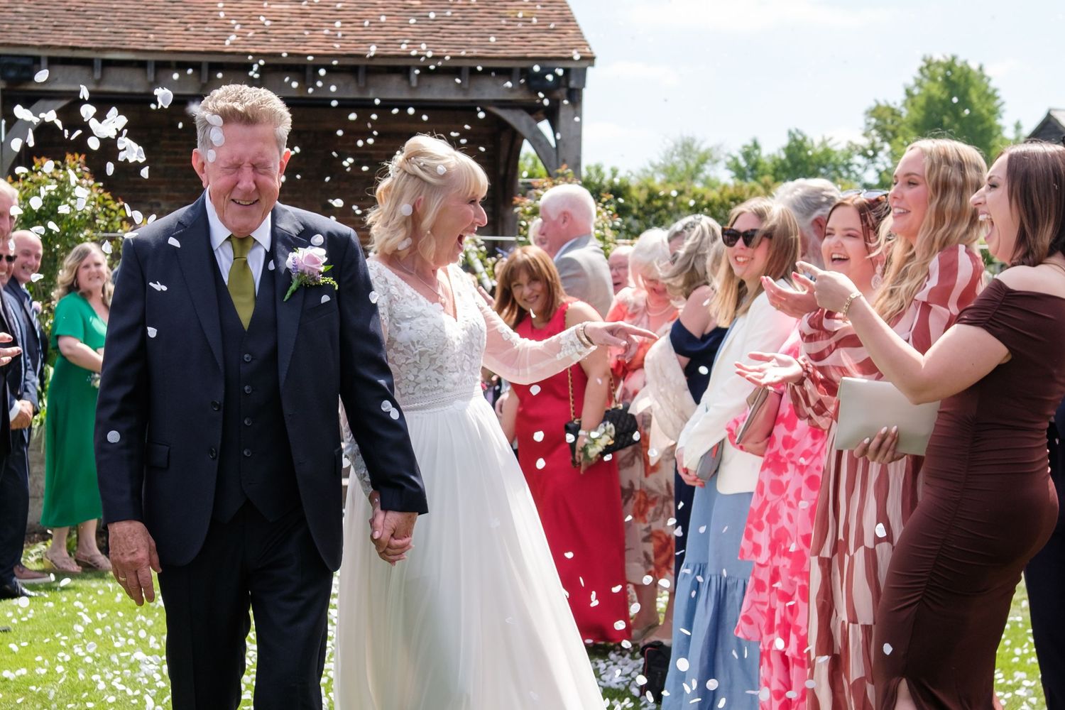 Wedding guests throw confetti over a couple outside during a sunny summer celebration in a garden setting.