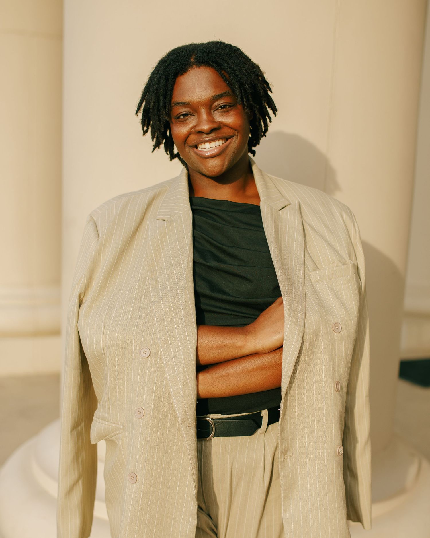 Person in a beige pinstripe suit and black top smiles confidently against a neutral background.
