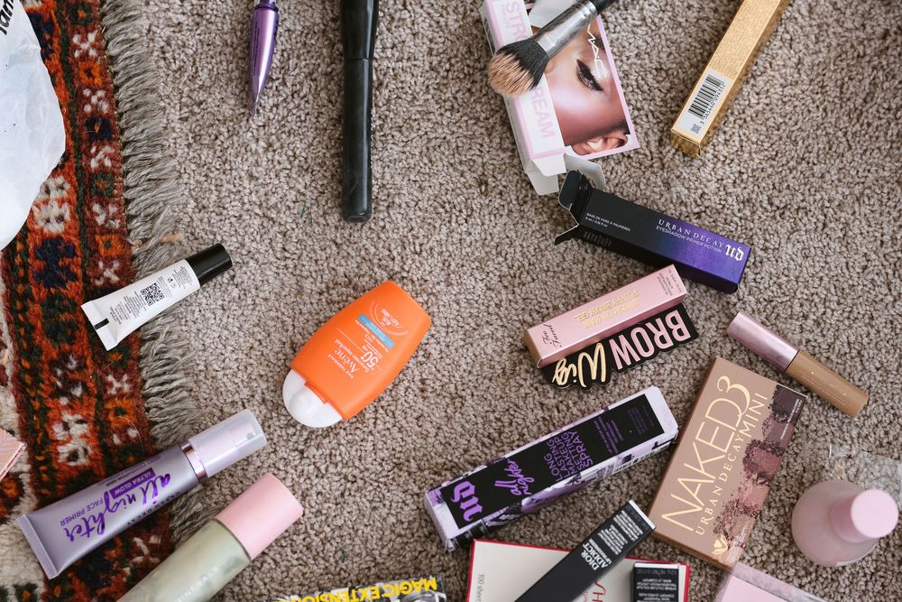 Various beauty and cosmetic products including makeup and beauty tools scattered on a gray textured surface.