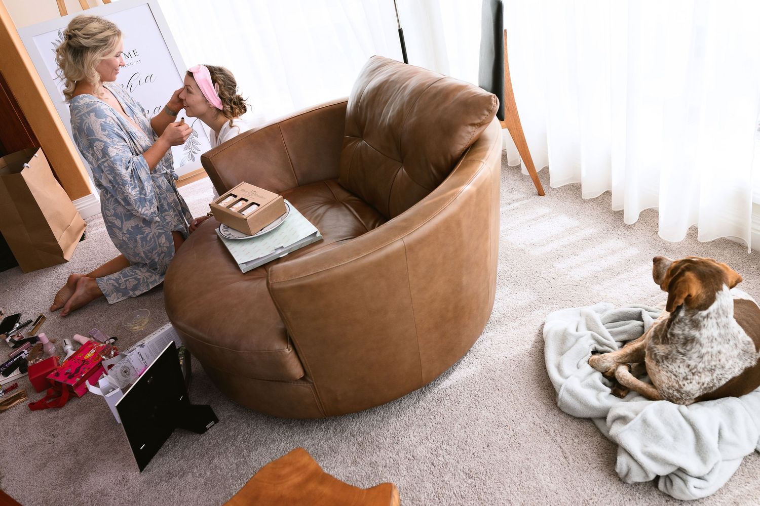 A cozy reading scene with a large brown circular chair, books scattered nearby, and a dog resting on blankets.