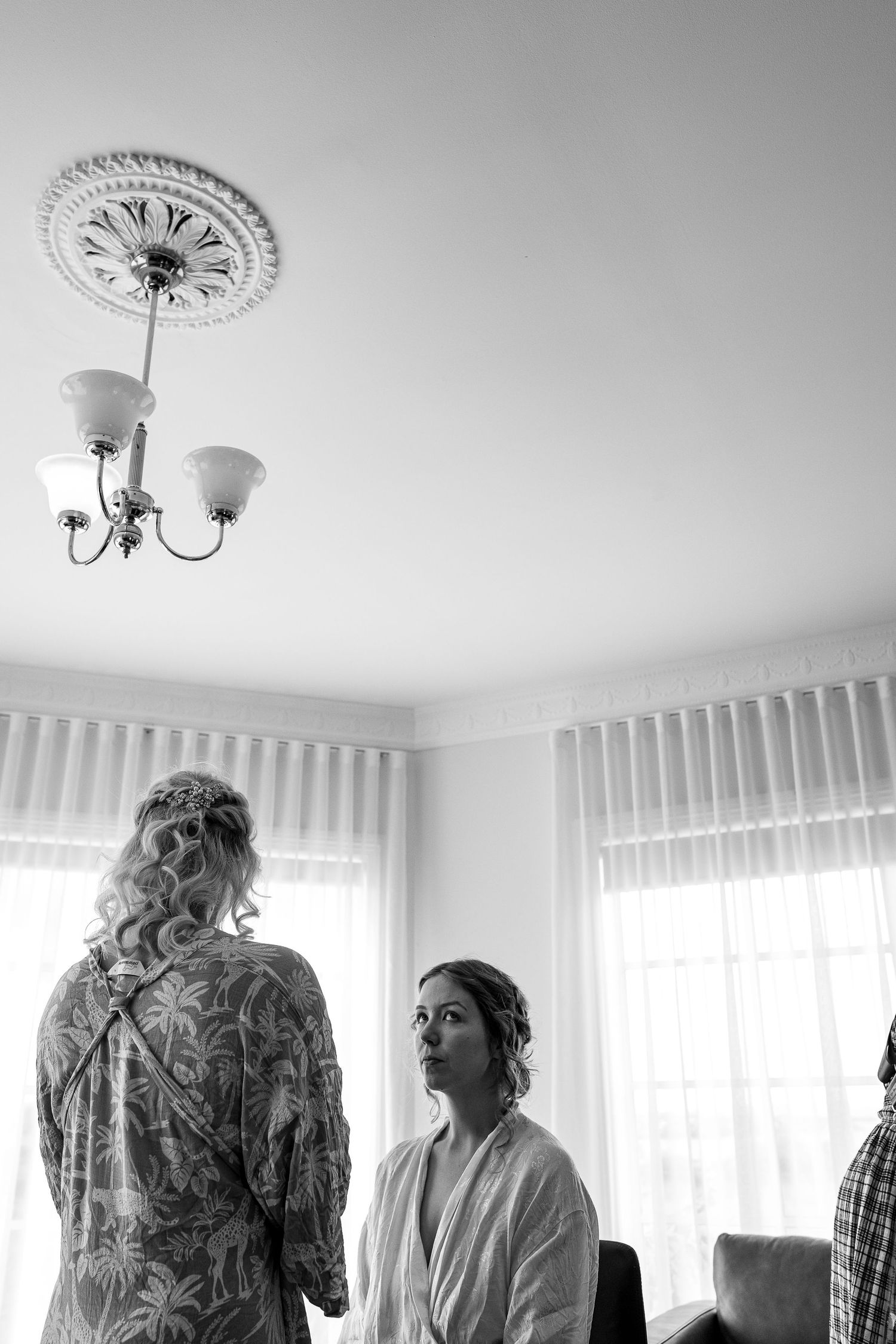 Black and white photo of a getting-ready scene with white curtains and a decorative ceiling light fixture in an interior room.