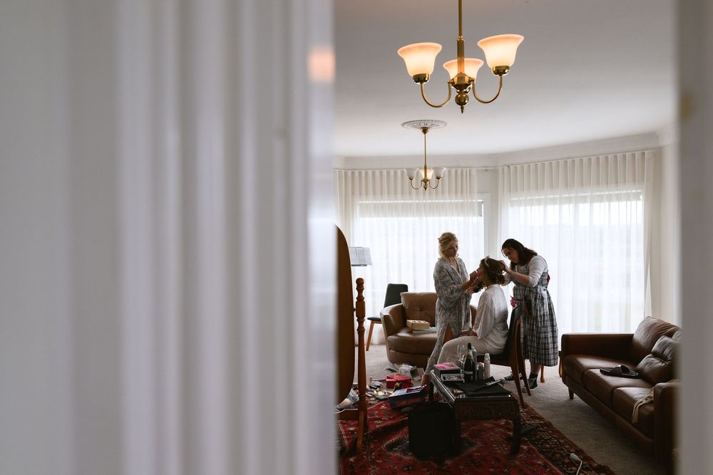 Silhouetted figures in a bright living room with chandelier and vintage furniture against window light.